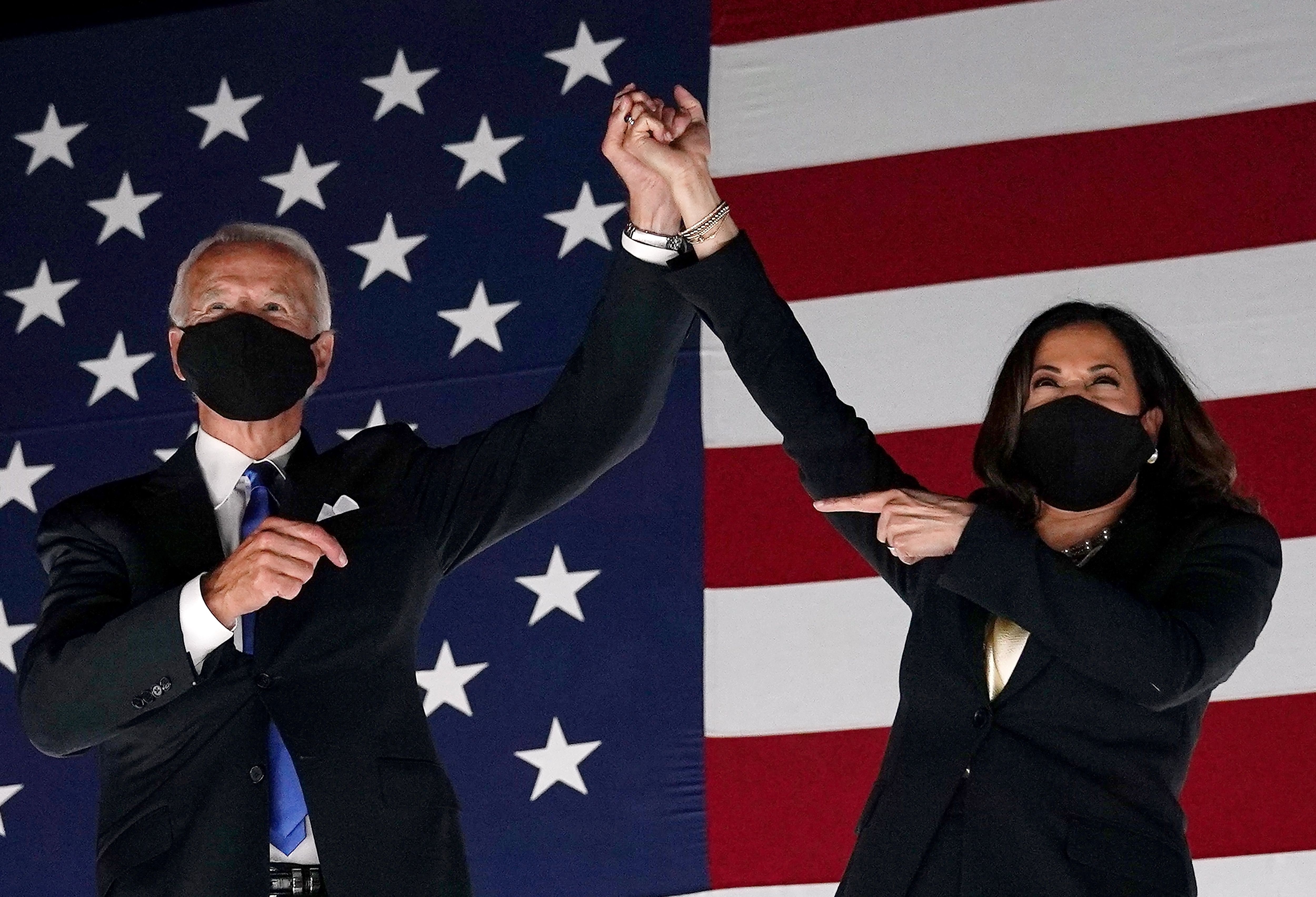 Joe Biden and Kamala Harris raise hands together in front of an American flag